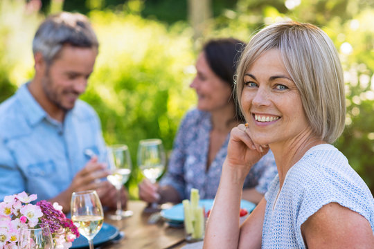 A group of friends gathered to share a meal around a table in the garden. Focus on a beautiful woman looking at the camera