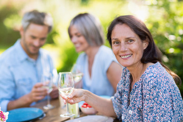 A group of friends gathered to share a meal around a table in the garden. Focus on a beautiful woman looking at the camera