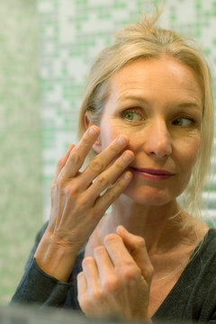 Mature woman scrutinizing her face in bathroom mirror