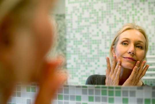 Mature woman scrutinizing her face in bathroom mirror