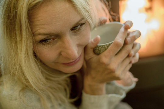Mature woman relaxing by fire with warm drink
