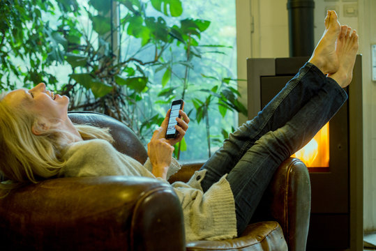 Mature woman laughing while relaxing at home with smartphone