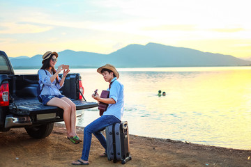 couple traveler playing guitar and watching sunset near the lake background  the mountain.Asia tourist enjoying for sunset during holiday