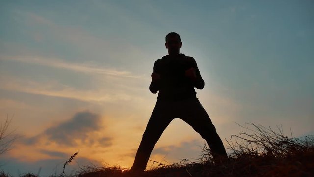 man warrior martial arts monk practicing silhouette karate kung Fu on the grassy horizon at sunset. Karate kick leg. Art of self-defense. Silhouette on a background of dramatic clouds at lifestyle