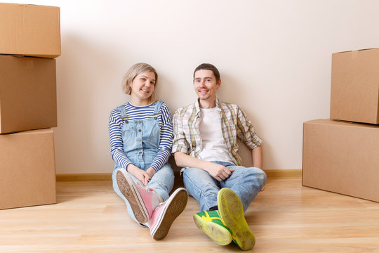 Photo of young married couple sitting on floor among cardboard boxes