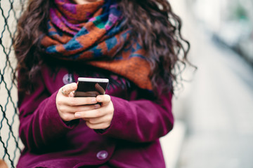 Girl standing agains t the wall on the street and using smart phone for texting.