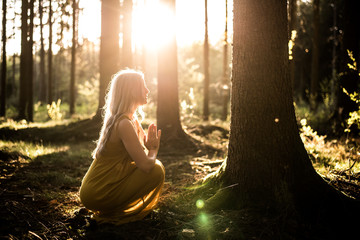 Junge Frau betet im Wald zum Sonnenuntergang - obrazy, fototapety, plakaty