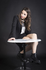 Studio portrait of a beautiful brunette sitting at a marble round table on black background