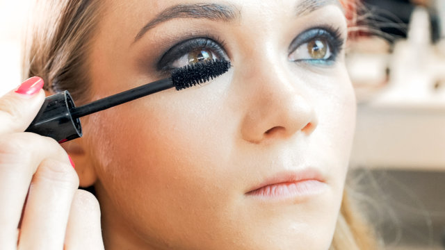 Closeup image of young blonde woman painting eyes with mascara