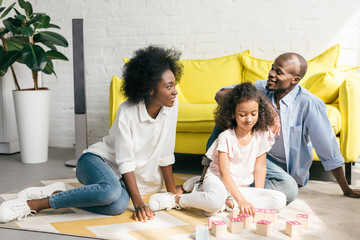 Fototapeta premium african american parents and daughter playing with wooden blocks together on floor at home