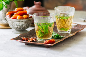 Traditional moroccan mint tea with dates on a vintage tray. White stone background.
