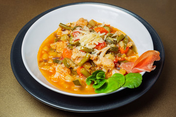 Italian Minestrone soup in a ceramic white bowl on a golden background