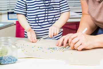 Mother and child make a pattern of beads on the fabric.