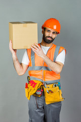 A man-builder in an orange helmet with a cardboard box in his hands. On a gray background