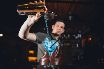 Barman mixes an alcoholic cocktail of blue color behind bar rack