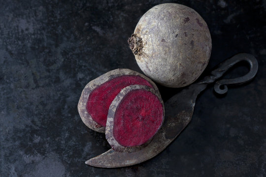 Whole and sliced beetroot and an old knife on dark metal
