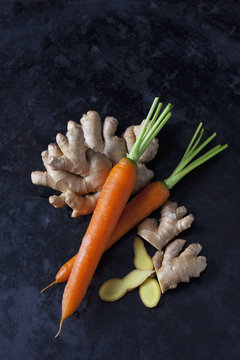 Overhead view of fresh ginger and carrots against black background
