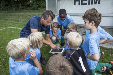 Coach with tablet and young football players on football ground
