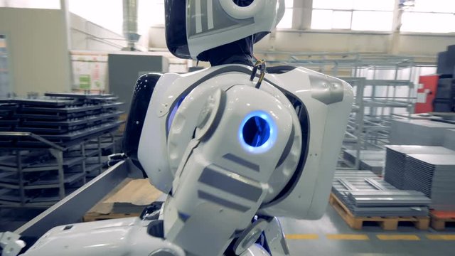 A white robot carries a metal item at a factory, close up.