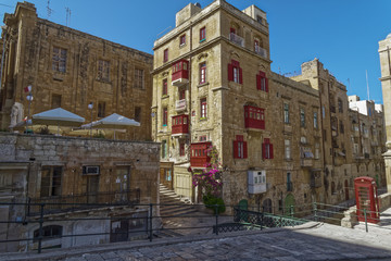 Valletta, Malta Traditional buildings with red balconies. Day view of Maltese limestone buildings with British phone booth in the streets of the capital of Malta.