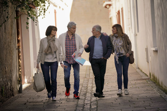 Group Of Senior Friends Walking In Street Of French Town