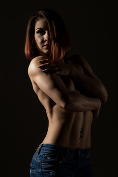 Young female model with muscular body poses on a dark background