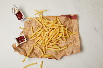 top view of french fries on crumpled paper with containers of ketchup on white