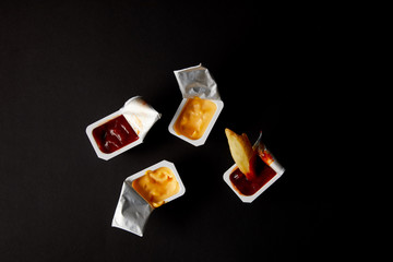 top view of plastic containers with sauces and poured french fry isolated on black