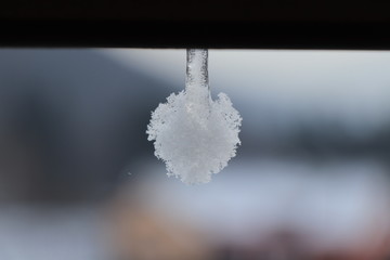 A  white frozen ball hanging on old gutter