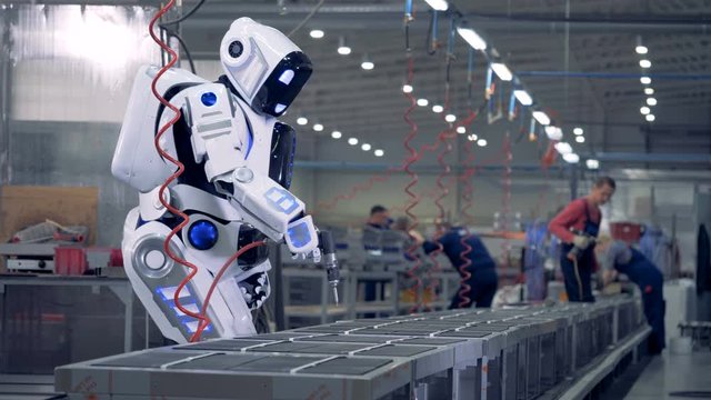 Human like robot works at a factory, using a special tool.