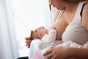 mother breastfeeding baby girl in white interior