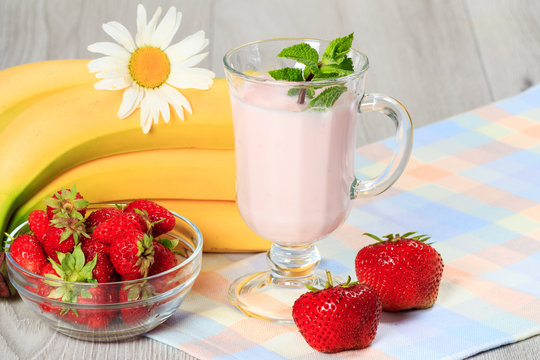 Glass of yogurt  with mint and fresh strawberries, banana, chamomile on the table