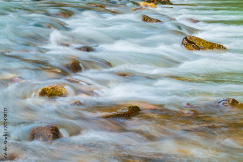 Motion Blurred Rapids Of Mountain River And Wet Boulders