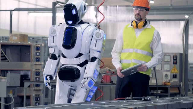 A factory worker switches on a droid, controlling it.
