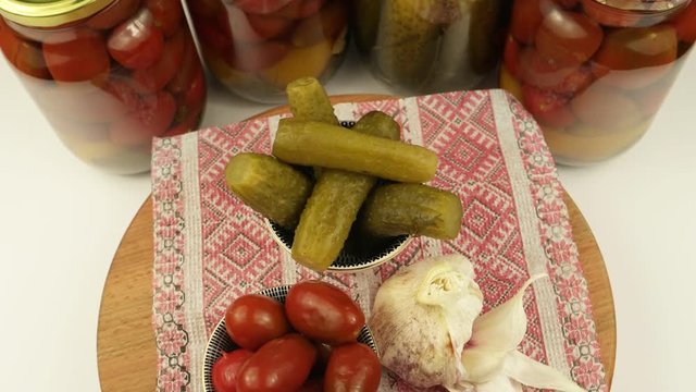 Two small bowls of the pickled tomatoes and cucumbers, garlic head on the background of glass cans with tomatoes and cucumbers