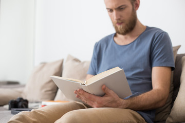 Close up photo of  man sitting on gray sofa and thoughtfully reading book at home isolated