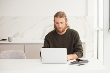 Portrait of young man sitting at the table and thoughtfully working on laptop at home isolated