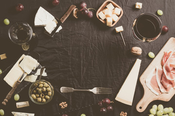 Palette of many types of cheese and some grapes, olives and wine with copy space.