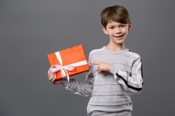 Christmas present. Positive cute boy holding a gift box while pointing at it