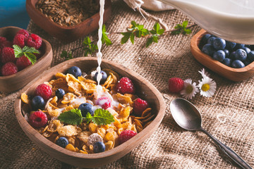 Cornflakes and other cereals with fresh fruits of raspberries, blueberries and pouring milk on healthy breakfast.