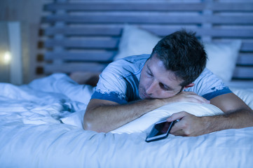 attractive tired man in bed falling asleep while using mobile phone still holding the cellular in his hand while sleeping in internet and social media addiction