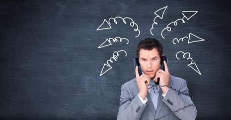 Stressed businessman on phones with arrow doodles on blackboard