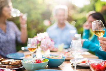 Focus on a colored salad in a bowl, Friends gather to share a meal around a table in the garden. Focus on the foreground