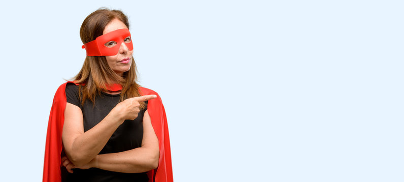 Middle age super hero woman wearing red mask and cape pointing away side with finger isolated blue background