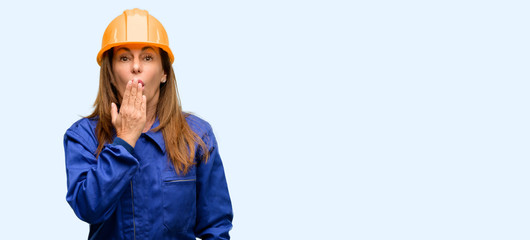 Engineer construction worker woman covers mouth in shock, looks shy, expressing silence and mistake concepts, scared isolated blue background