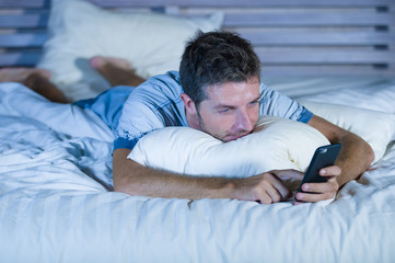 young attractive and happy man lying on bed using internet mobile phone smiling sending text in social media and cellular communication addiction