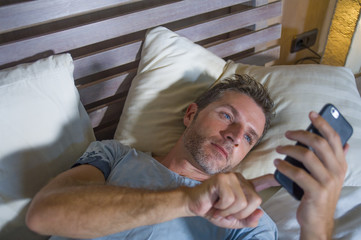 young attractive and happy man lying on bed using internet mobile phone smiling sending text in social media and cellular communication addiction