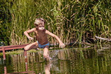 Little boy having fun and jumping into the river from pier