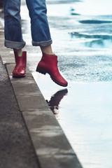 woman with red short boots standing on sidewalk next to a puddle of rain