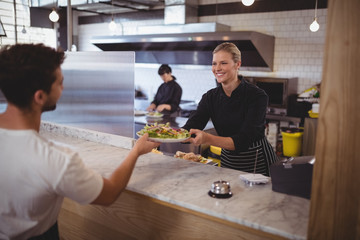 Smiling female chef giving fresh Greek salad to waiter